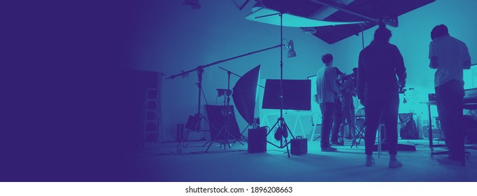 Two Tone Images Of Behind The Scene Of Photo Shooting Production Set Up In The Big Studio. Professional Crew Team Working And Camera Equipment In Silhouette. And Copy Space Added.