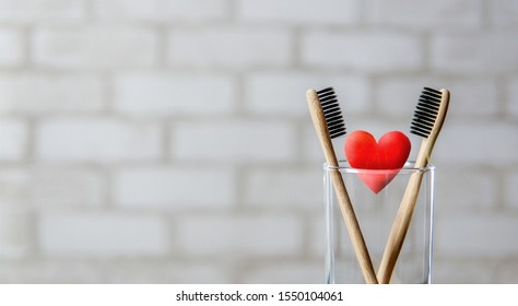 Two toothbrushes in the glass and red heart over brick wall background. Love and Valentines Day concept. Bamboo eco friendly toothbrushes