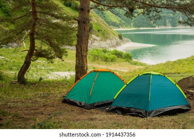 two tourist tents in a forest under a tree on a background of a lake and mountains. camping