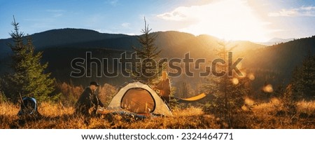 Two tourists pitch tent in the mountains at sunset. Family vacation in mountains.