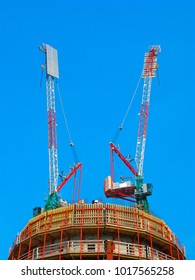Two tower cranes on top of a building under constraction on clear blue sky. Also on photo are constration scaffolding and iron armature sticking out of concrete formwork.