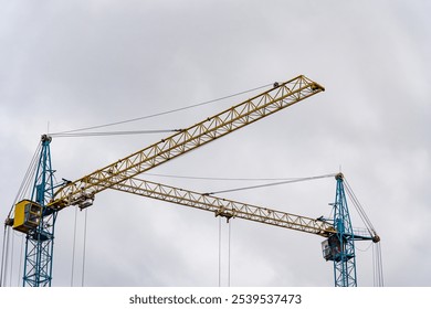 Two towering construction cranes are actively engaged in the building process of a new house, surrounded by a cloudy sky in the early morning - Powered by Shutterstock