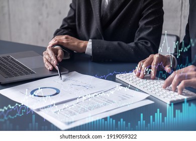 Two traders man and woman researching historic data to predict stock market behavior. Internet trading concept. Forex and financial hologram chart over the table with the documents