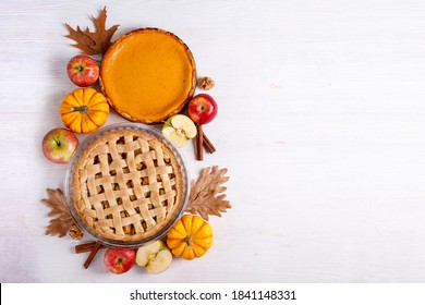 Two traditional American Thanks Giving pies with apples, mini pumpkins & cinnamon sticks. Homemade fruit tarts baked to golden crust. Close up, copy space, top view, background.