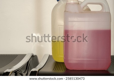 Two translucent gallon containers filled with pink and yellow floor cleaning liquids, placed side by side on a black surface. Ideal for sanitation and industrial cleaning purposes.