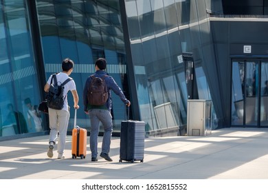 Two Traveler Guys Go To The Airport Entrance With Suitcases Rear View