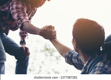 Two travelers are pulling their hands together to help their friends up. - Shutterstock ID 1377387281