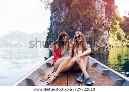 Two traveling women, best friends exploring wild nature of Khao Sok national park.  Sitting in wood long tail boat on tropical limestone cliffs background. Lifestyle image. Island lagoon.