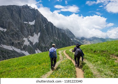 Two trekker walking past Gadsar lake and a meadow at kashmir great lakes trek in kashmir. Solo person in the mountains and lake of Kashmir, India. The breathtaking view of Krishansar lake on blue sky.