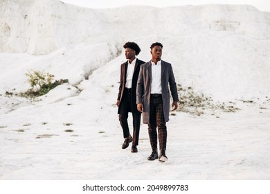 Two trendy african american men, in classic black suits and polts, men posing together outdoors against the backdrop of white chalk mountains, fashion posing concept, mens autumn clothing, style