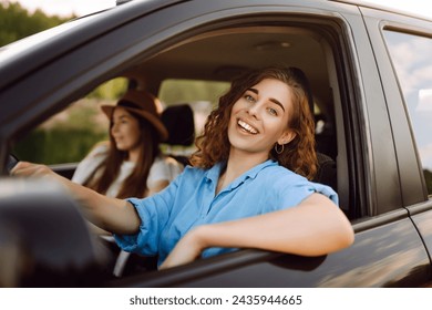 Two trendy attractive young woman singing along to the music as they drive along in the car through town. Beautiful female friends in the car enjoy a car trip together. - Powered by Shutterstock