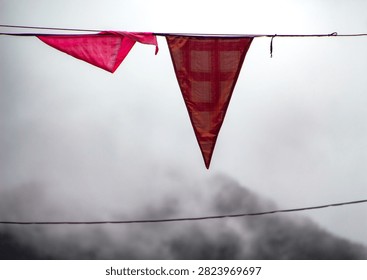 Two triangular red flags hanging on a wire against a foggy mountain backdrop.