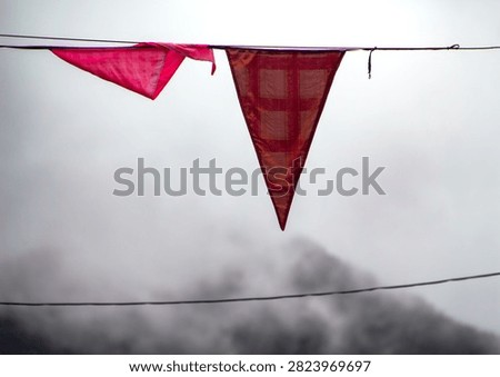 Two triangular red flags hanging on a wire against a foggy mountain backdrop.