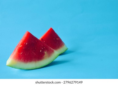 Two triangular watermelon wedges placed on the left side of a clean blue background with extensive right-side copy space.