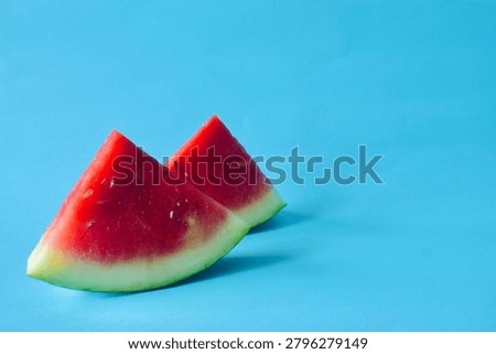 Two triangular watermelon wedges placed on the left side of a clean blue background with extensive right-side copy space.