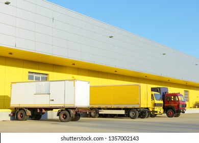 Two truck trailers and two trucks parked in front of a yellow factory .  - Shutterstock ID 1357002143
