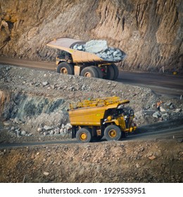 Two trucks in a modern gold mine in Australia. Large haul trucks transport gold ore from the pit. Water truck following haul truck uphill of open cast mine.