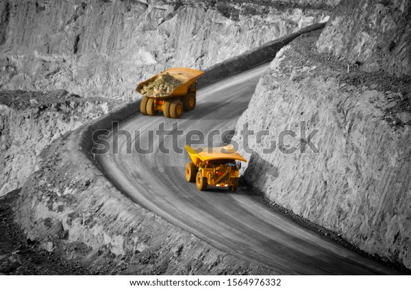 Two trucks in a modern gold mine in Australia.\
Spot color large haul trucks transport gold ore from the pit, Open\
cast mine. Yellow trucks, black and white background. - All logos\
removed.
