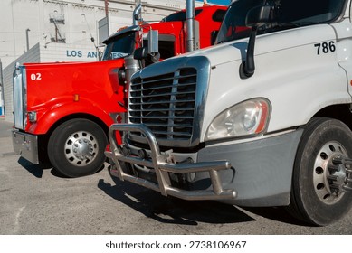 Two trucks are parked side by side in a Los Angeles area. One truck is red, while the other is white. The vehicles are positioned on a paved surface.