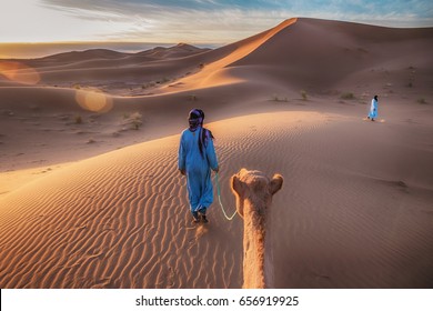 Two Tuareg nomads leading a camel in the Sahara Desert, Morocco.