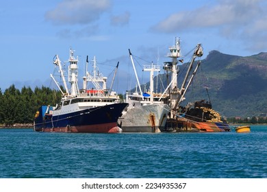 Two tuna boats are moored to a cargo ship in the harbor. - Shutterstock ID 2234935367