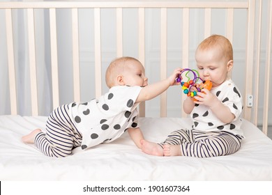two twin babies play in the crib, the concept of the relationship of children of brother and sister, the child takes the toy from the other