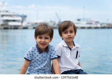 Two twin brothers of the model are sitting next to each other in fashionable clothes on the background of the sea.