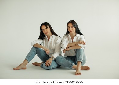 Two Twin Sisters In White Shirts And Blue Jeans