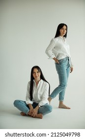 Two Twin Sisters In White Shirts And Blue Jeans