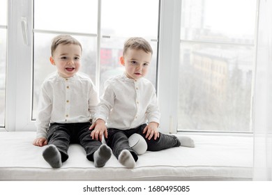Two two-year-old twin boys in white shirts and black pants posing in front of the camera.