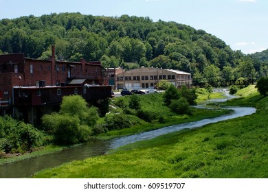 Two Ugly Buildings On The Edge Of A Small Appalachian Town Sit Beside The Bank Of A Beautiful Small River Winding Through The Hills And Woods Of A Beautiful Surrounding Landscape.