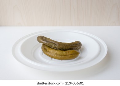 Two Ugly Fermented Pickles Are Rotting On A White Plate