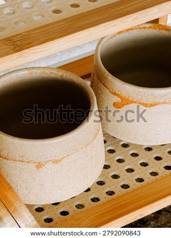 Two unglazed earthenware cups with orange speckles rest on a perforated white mat. They are positioned on a bamboo drying rack, likely air drying.