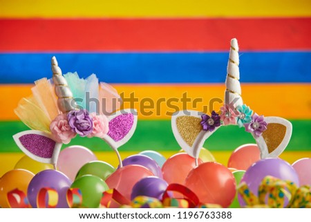 Two unicorn headbands in pile of multicolored balloons in front of brightly colored striped background