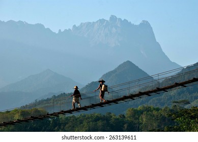 Two unidentified couple of elderly farmers at Kota Belud, Sabah are walking on a suspension bridge on an early morning, with Mount Kinabalu as background - Powered by Shutterstock