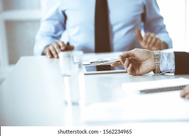 Two unknown businessmen or partners using tablet pc and discussing questions at meeting in modern office, close-up of hands. Group of managers at negotiation or brainstorm. Teamwork, partnership and