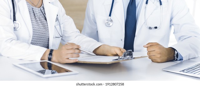 Two unknown doctors discussing treatment problems while sitting at the desk in hospital office, close-up. Data in medicine