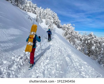 Two unrecognizable active tourists snowshoe up a scenic hiking trail in the sunny Julian Alps. Snowboarder and ski tourer trek up a hill to shred the ungroomed slopes in the idyllic Slovene mountains.