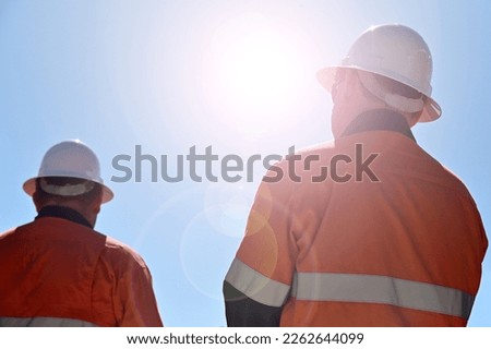 Two unrecognizable blue collar workers isolated against clear blue sky with sun flare.Real people. Copy space 