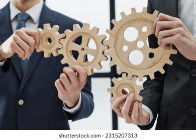 two unrecognizable businessmen are holding wooden cogwheels. - Shutterstock ID 2315207313