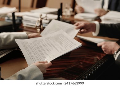 Two unrecognizable caucasian business people exchanging documents sitting at wooden desk in office - Powered by Shutterstock