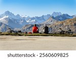 two unrecognizable cyclists sit and look at the high mountains