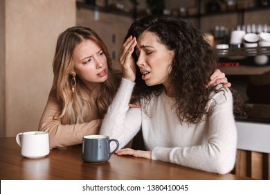 Two Upset Young Girls Friends Sitting At The Cafe Table, Drinking Coffee, Cheering Each Other Up