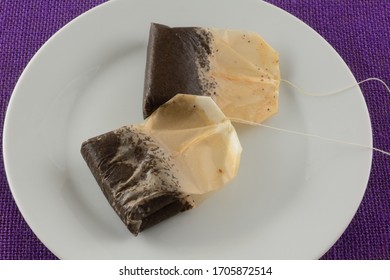 Two Used Black Tea Teabags On White Plate On Purple Tablecloth After Making Iced Tea