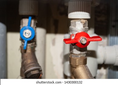 Two valves on plastic and metal pipes with hot and cold water. Open blue and closed red switches. Hot water is turned off. Closeup view