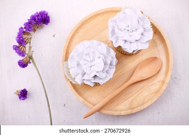 Two Vanilla Cupcakes With Purple Buttercream In Blossom Shape On Wooden Dish, And Be Dry Statice Flower