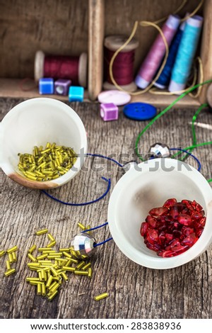 two vases with small beads on the background of tools for needlework.Selective focus.Photo tinted