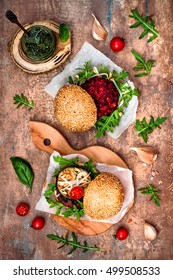 Two Veggies Burgers Served On Cutting Board Over Stone Vintage Background. Vegan Grilled Eggplant, Arugula, Sprouts, Pesto Sauce Burger. Veggie Beet And Quinoa Burger. Top View, Overhead, Flat Lay. 