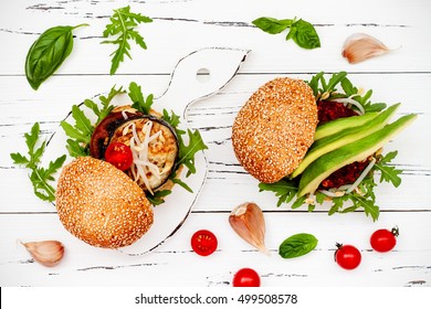 Two Veggies Burgers Served On Cutting Board Over White Rustic Table. Vegan Grilled Eggplant, Arugula, Sprouts And Pesto Burger. Veggie Beet And Quinoa Burger With Avocado. Top View, Overhead, Flat Lay