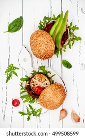 Two Veggies Burgers Served On Cutting Board Over White Rustic Table. Vegan Grilled Eggplant, Arugula, Sprouts And Pesto Burger. Veggie Beet And Quinoa Burger With Avocado. Top View, Overhead, Flat Lay